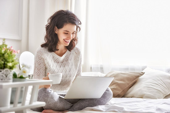 woman smiling with cup looking at laptop